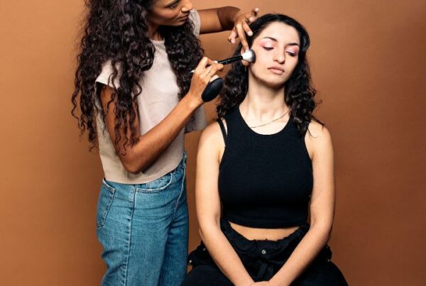 Close-up of a MAC makeup artist applying dramatic eyeshadow on a model with bold lighting and a professional makeup setup in the background.