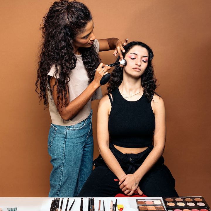 Close-up of a MAC makeup artist applying dramatic eyeshadow on a model with bold lighting and a professional makeup setup in the background.