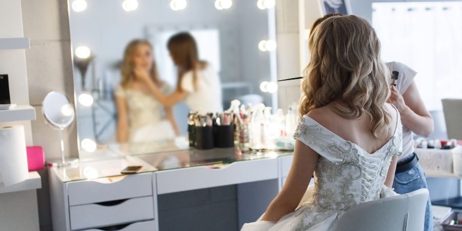 Bride getting her makeup done at a vanity mirror, reflecting the essential questions makeup artists ask to ensure the perfect bridal look.