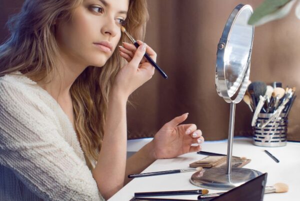 A makeup student uses her Makeup Artistry Kit to apply eyeshadow in front of a vanity mirror, with professional brushes, palettes, and cosmetics neatly arranged on the table.