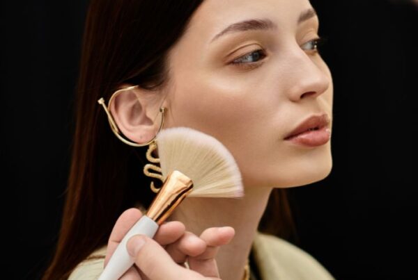 Makeup artist applying powder to a model’s cheek with a fan brush, capturing a behind-the-scenes moment that reflects the hands-on, creative nature of careers in makeup artistry.