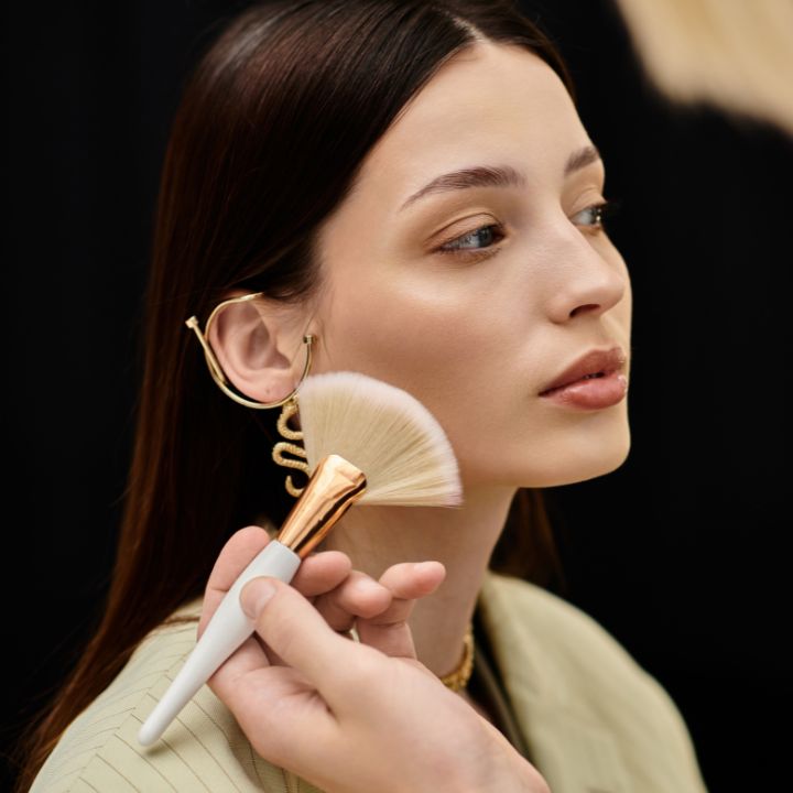 Makeup artist applying powder to a model’s cheek with a fan brush, capturing a behind-the-scenes moment that reflects the hands-on, creative nature of careers in makeup artistry.
