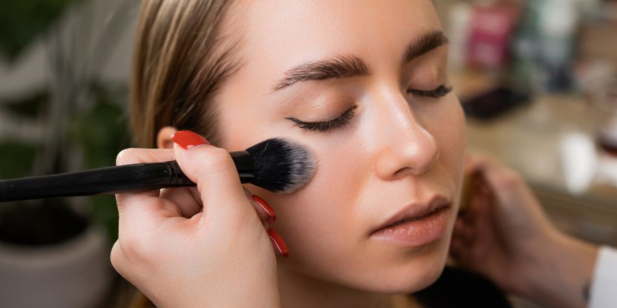 Makeup artist applying blush to a model’s cheek with a fluffy brush—showcasing hands-on skills essential for successful careers in makeup artistry.