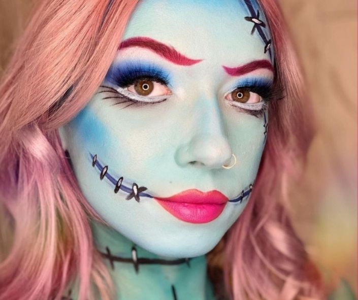 Creative Halloween makeup idea featuring a stitched doll look with blue face paint, pink hair, bold eye makeup, and bright lipstick for a spooky yet stylish effect.