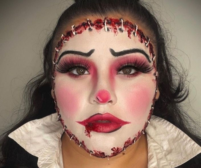 Scary Halloween makeup featuring a stitched doll face design with fake blood, dramatic lashes, and bold red accents for a creepy special effects look.