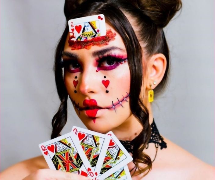 Creative Halloween makeup idea featuring a Queen of Hearts look with stitched lips, bold red accents, dramatic eye makeup, and playing card props.