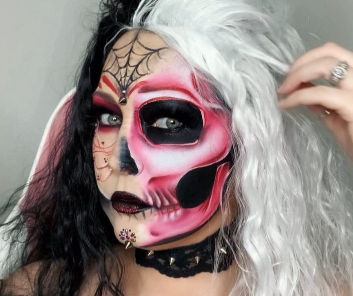 Scary Halloween makeup featuring a half-skull face design with red and black shading, spiderweb details, and a dramatic black-and-white wig for a bold gothic look.