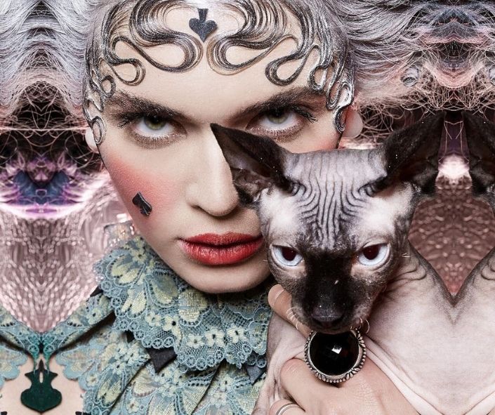 Creative Halloween makeup idea featuring an elegant gothic queen look with heart-shaped designs, vintage lace costume, and a Sphynx cat for a dramatic effect.