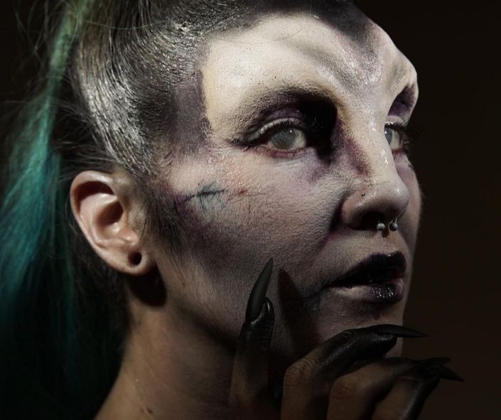 Scary Halloween makeup featuring a demonic-inspired look with pale textured skin, eerie white contact lenses, black claws, and dark lipstick for a haunting effect.