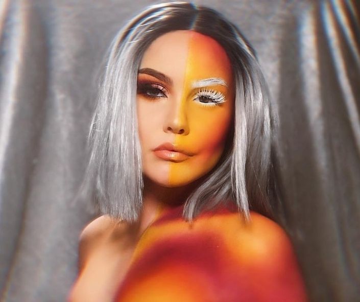 Creative Halloween makeup idea featuring a split-face design with fiery orange and yellow tones on one side, dramatic dark eye makeup on the other, and bold silver hair for a striking contrast.