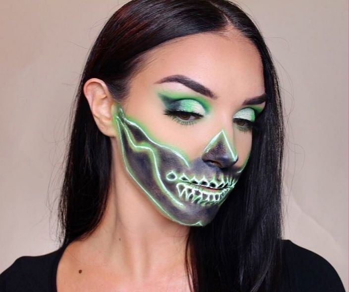Creative Halloween makeup idea featuring a neon green skeleton design with glowing face paint, bold black shading, and matching green eye makeup for a striking look.