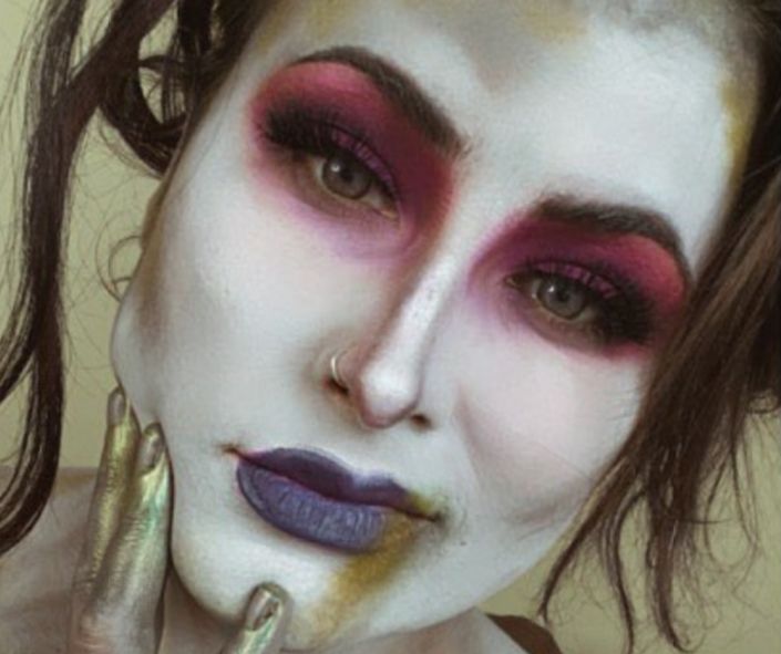 Creative Halloween makeup idea featuring bold pink eye makeup, white face paint, purple lips, and golden hand accents for a mystical fantasy-inspired look. Beetlejuice makeup.