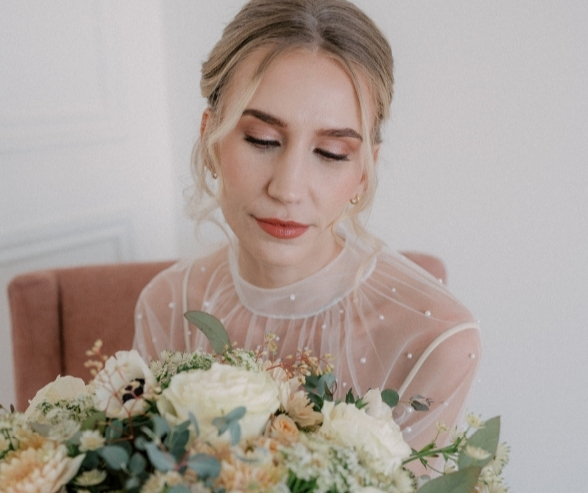 Soft and romantic traditional bridal makeup look featuring warm eyeshadow, peach lipstick, and a sheer pearl-detailed gown.
