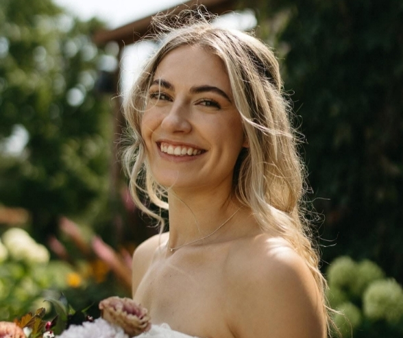 Smiling bride with natural makeup and flowing blonde hair in a garden setting, showcasing effortless makeup ideas for bride with a fresh, radiant glow.