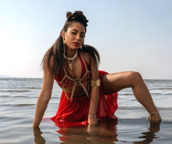 Model posing in the ocean wearing a red dress and gold accessories, featuring bold eye makeup and glowing skin that reflect creative makeup inspiration and artistry. Makeup by QC Makeup Academy student, Kate Loveland.