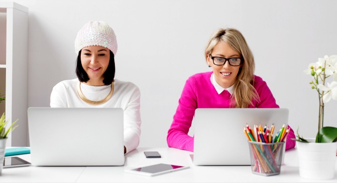Two young women using laptops