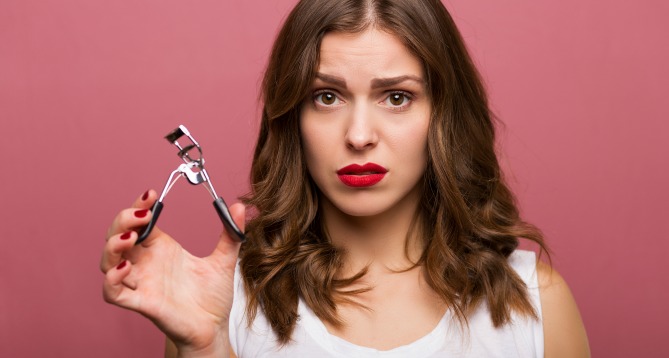 Hesitant and tough makeup client holding eyelash curlers
