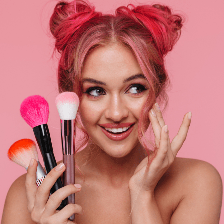 Portrait of beautiful shirtless woman with colorful hairstyle holding makeup brushes isolated over pink background
