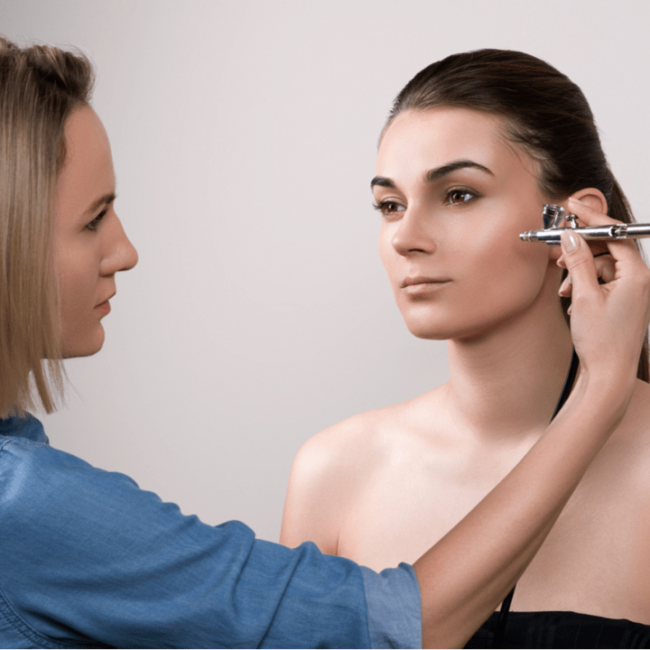 MUA using airbrush on female model's face