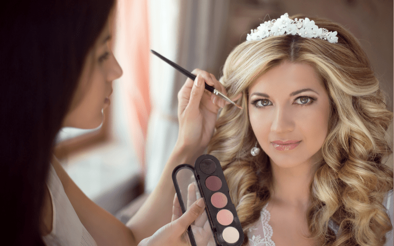 makeup artist equipped with a makeup palette applying makeup on bride