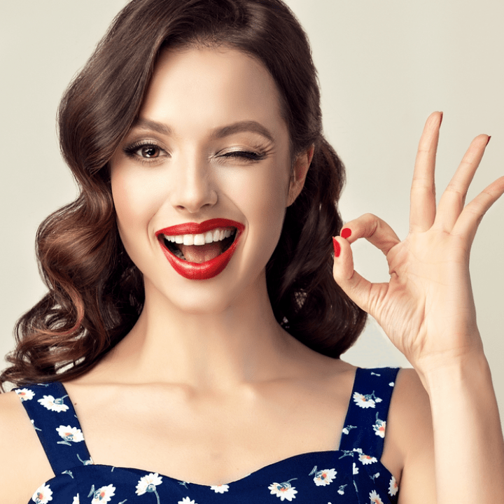 woman with pinup-style hair and makeup winking and giving OK sign with hand