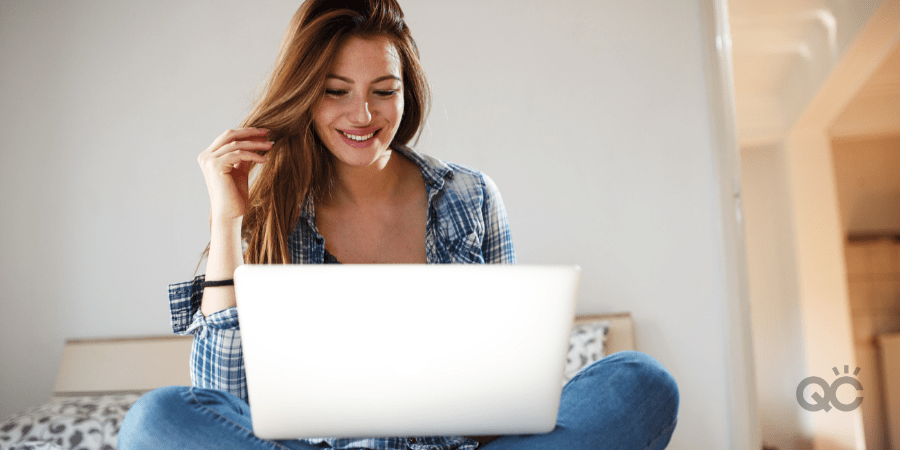 smiling girl sitting on bed with laptop on lap