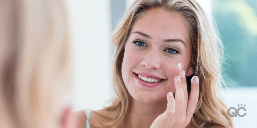 Smiling pretty woman applying cream on her face in bathroom