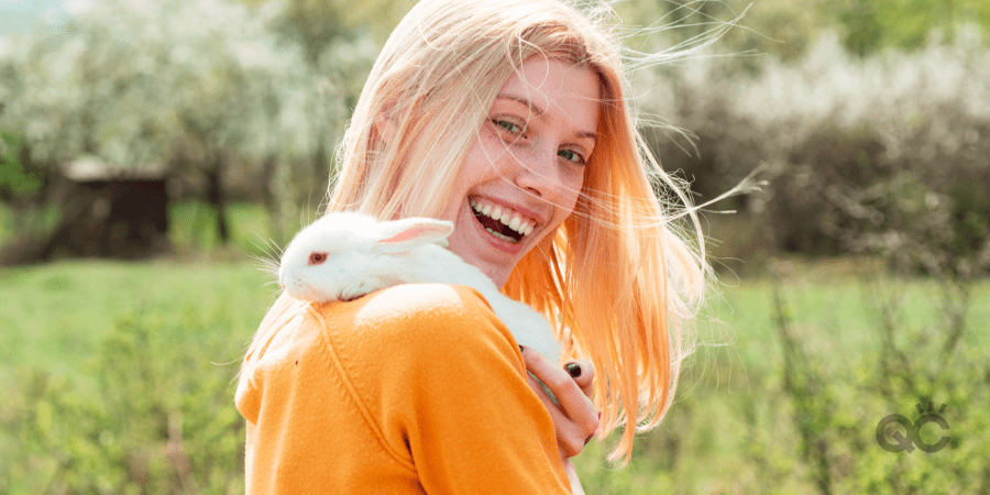 Funny girl hold rabbit on green field background. Closeup of winking girl with bunny rabbit. Lovely woman hold white rabbit