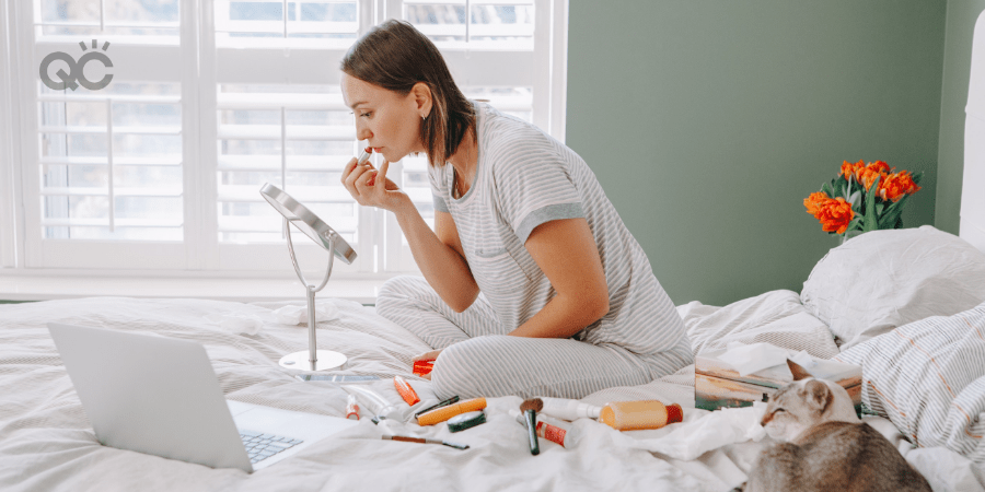 woman attending online makeup schools doing makeup on bed at home