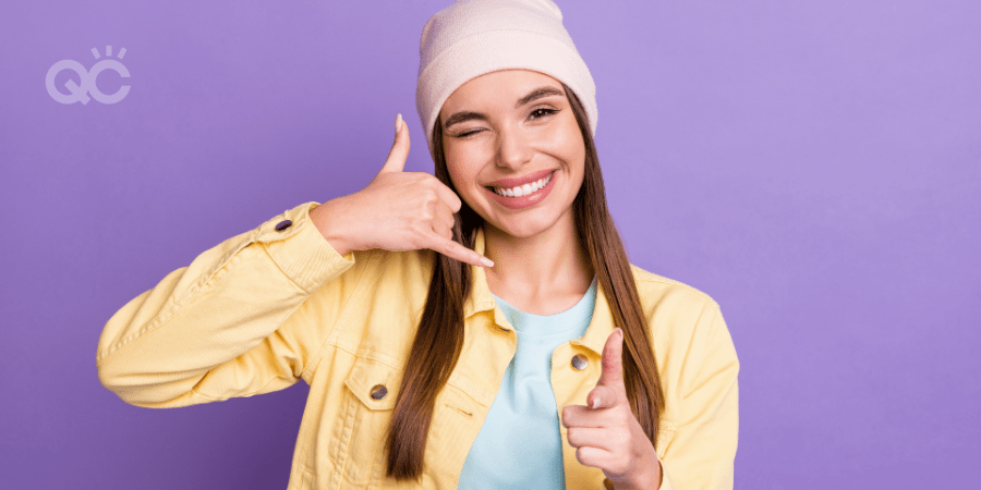 Photo portrait of funky young woman smiling cheerful showing call me sign winking blinking isolated on pastel purple color background