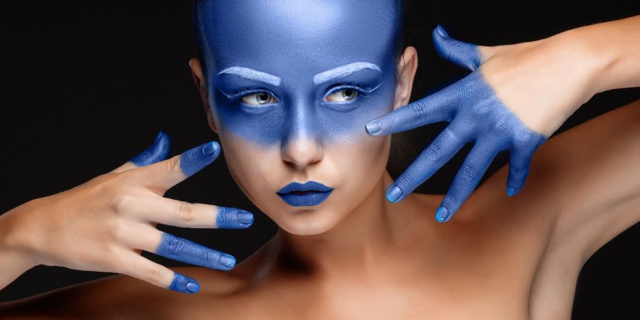 Portrait of a young woman who is posing covered with blue paint in the studio on a black background. girl's hands around the face and painted blue. Airbrush makeup article.
