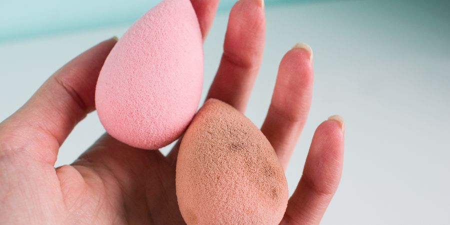 Pink beauty tear-shaped blender, dirty and clean egg-shaped sponges isolated on light background. Cosmetic tool for makeup in hand. Makeup and skincare products article.