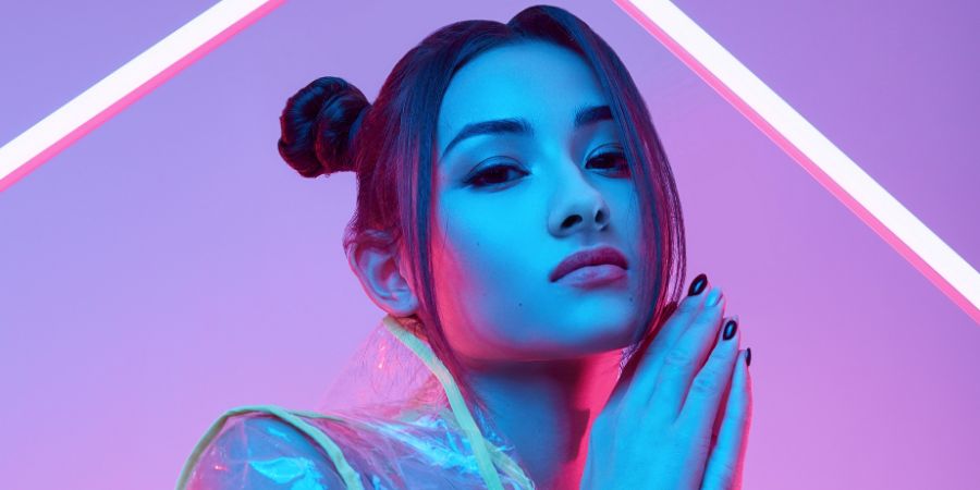 Portrait of elegant beautiful Asian woman in a fashionable raincoat around colourful bright neon uv lights posing in studio. Makeup photoshoot article.