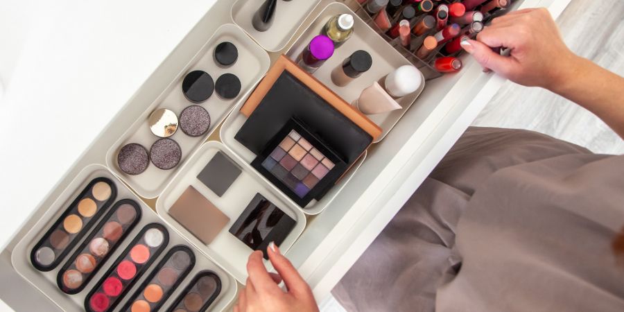 Woman hands neatly organizing makeup or cosmetics in the drawer of vanity dressing table and leaving her jewellery on dressing table surface. Visagiste is taking out vanity case of cosmetic powders. Makeup artist insurance article.
