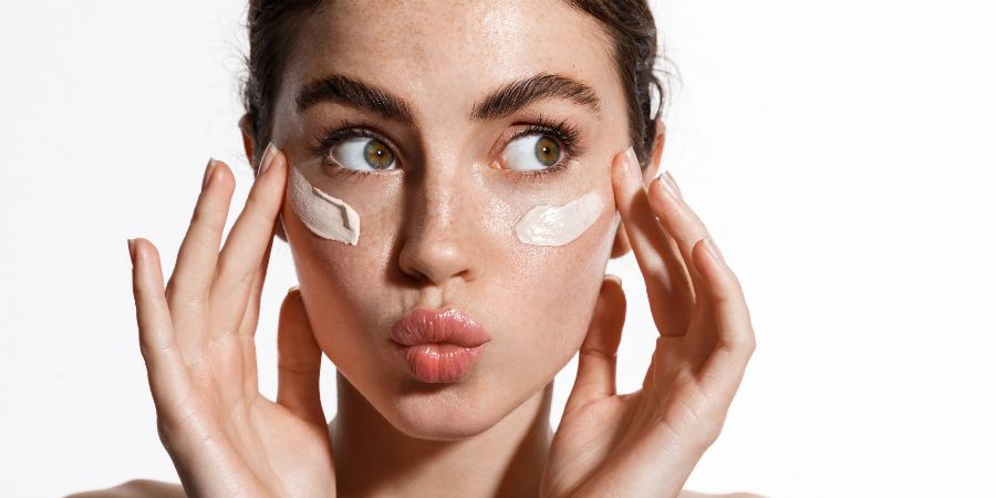Close up beauty girl with freckles and thick eyebrows, applying moisturizing skincare cream, lotion or mask for skin lifting and anti-aging detoxifying effect, white background. Makeup article.